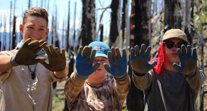 Three young people wearing gloves show them to the camera during a service project with outward bound. 